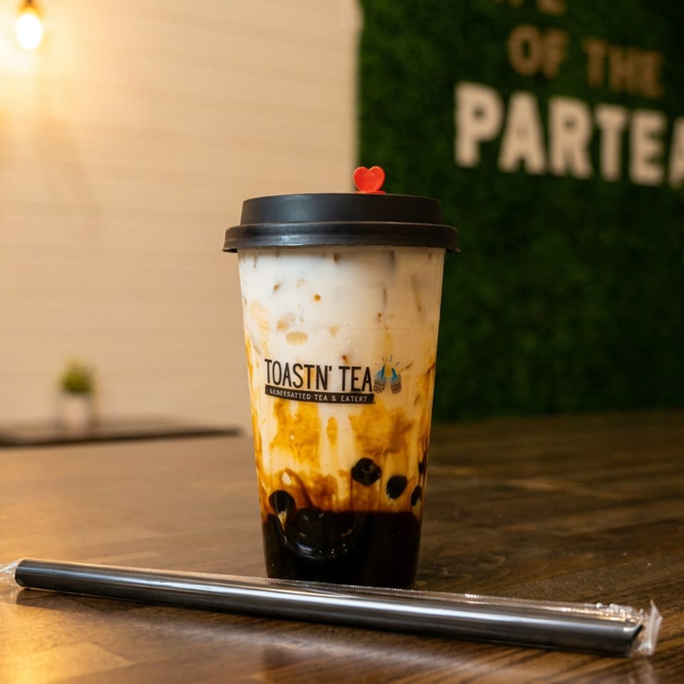Toastn' Tea boba drink with a red heart on the lid, and a straw on a wooden table.