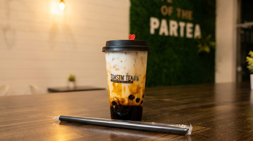 Toastn' Tea boba drink with a red heart on the lid, and a straw on a wooden table.