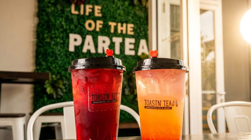 Two Toastn' Tea drinks, one red and one orange, on a table with a "Life of the Partea" sign.