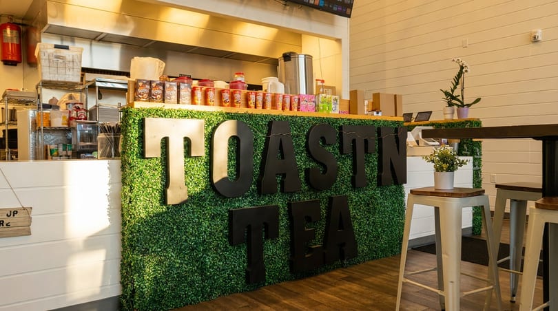 Interior of Toastin' Tea with a green hedge wall, counter, and bar stools.