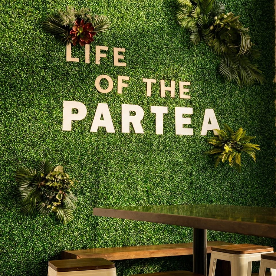 Green faux-grass wall with "LIFE OF THE PARTEA" in wooden letters, next to a table and benches.