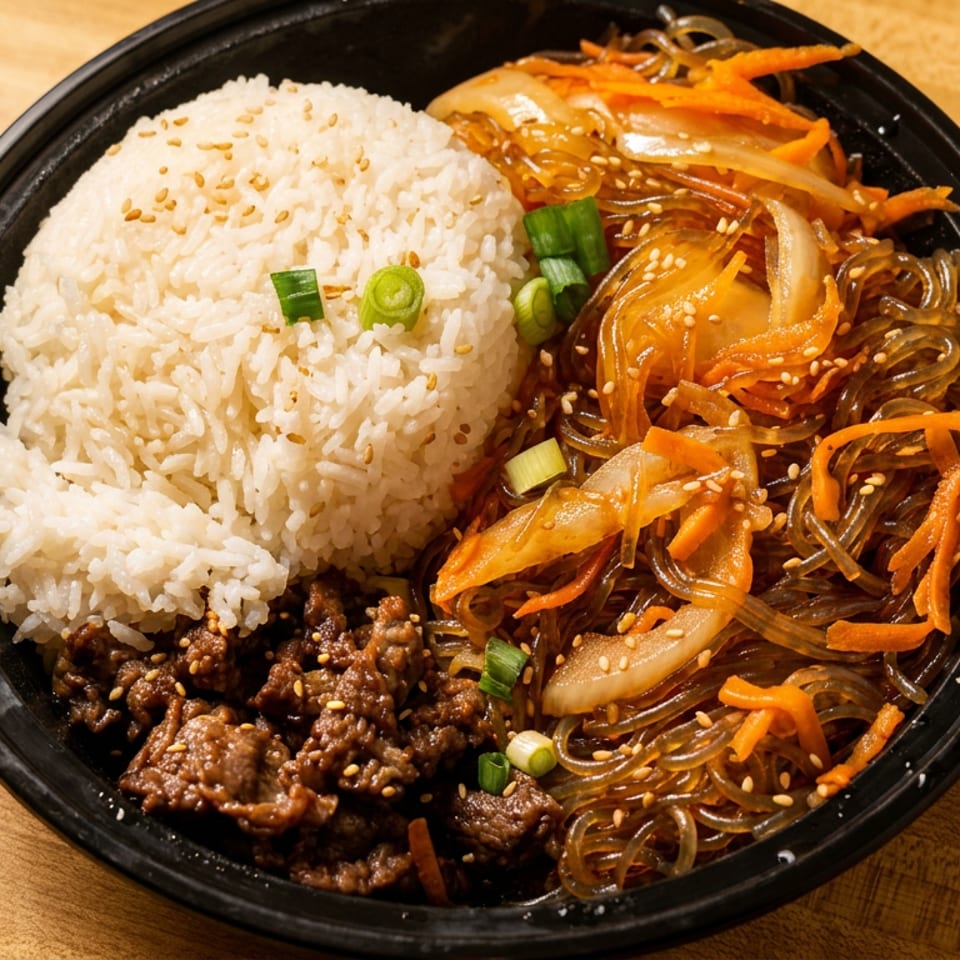 A black bowl filled with white rice, bulgogi beef, and japchae noodles with vegetables.