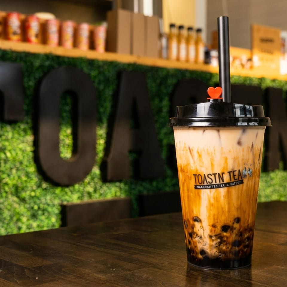 Toastn' Tea boba drink with a heart-shaped stopper on a wooden table, green wall in background.